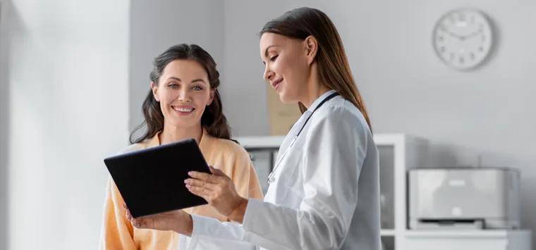 Ärztin zeigt einer Patientin etwas auf einem Tablet.