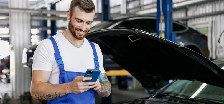 KFZ-Mechaniker schaut in der Werkstatt auf sein Smartphone.